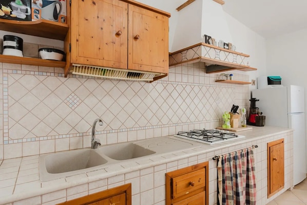 A kitchen with two sinks, wooden cabinets, a gas stove, and a refrigerator. - Charming Villa Rental in Mazara Del Vallo With Pool Access (Mazara del Vallo)