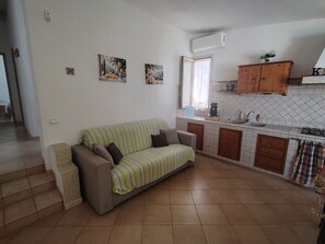 A living room with a sofa and a kitchen area with cabinets and a sink. - Charming Villa Rental in Mazara Del Vallo With Pool Access (Mazara del Vallo)