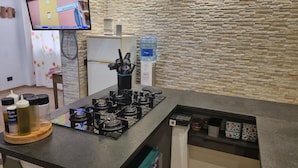 A kitchen with a gas stove, a water dispenser, and a television mounted on the wall. - Charming Villa Rental in Mazara Del Vallo With Pool Access (Mazara del Vallo)