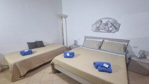 Habitación de hotel con dos camas individuales, cada una con cubrecama color beige y toallas azules. Sobre las camas hay una obra de arte colgada en la pared y una mesita de noche con una lámpara y un objeto decorativo.