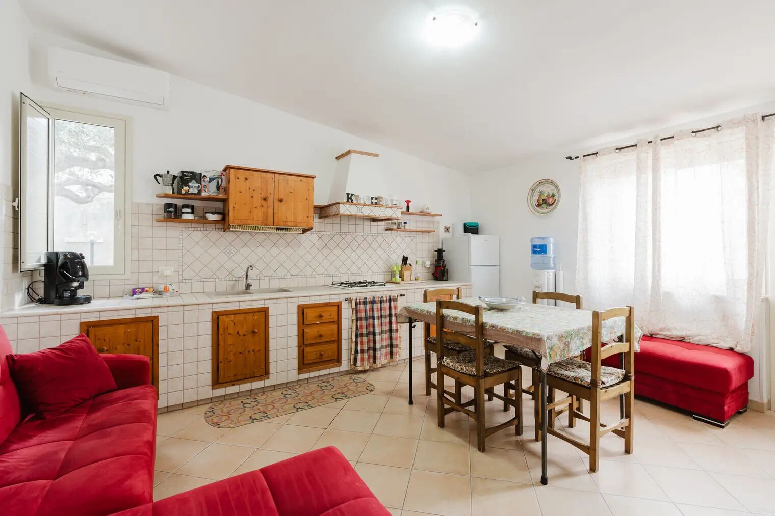 Cozinha compacta com armários de madeira, uma mesa de jantar e um sofá vermelho.