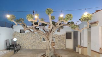 Uma árvore com várias luzes em um pátio com paredes de pedra e móveis de exterior.