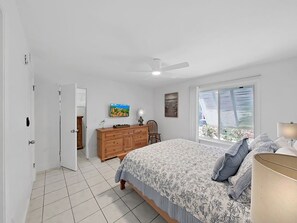 Ein Schlafzimmer mit Bett, Kommode, Deckenventilator und einem Fenster mit Jalousien.