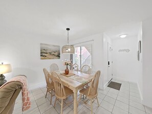 Ein Essbereich mit einem Holztisch, sechs Stühlen, einer Hängeleuchte, einer Vase mit Blumen und einem Gemälde an der Wand.