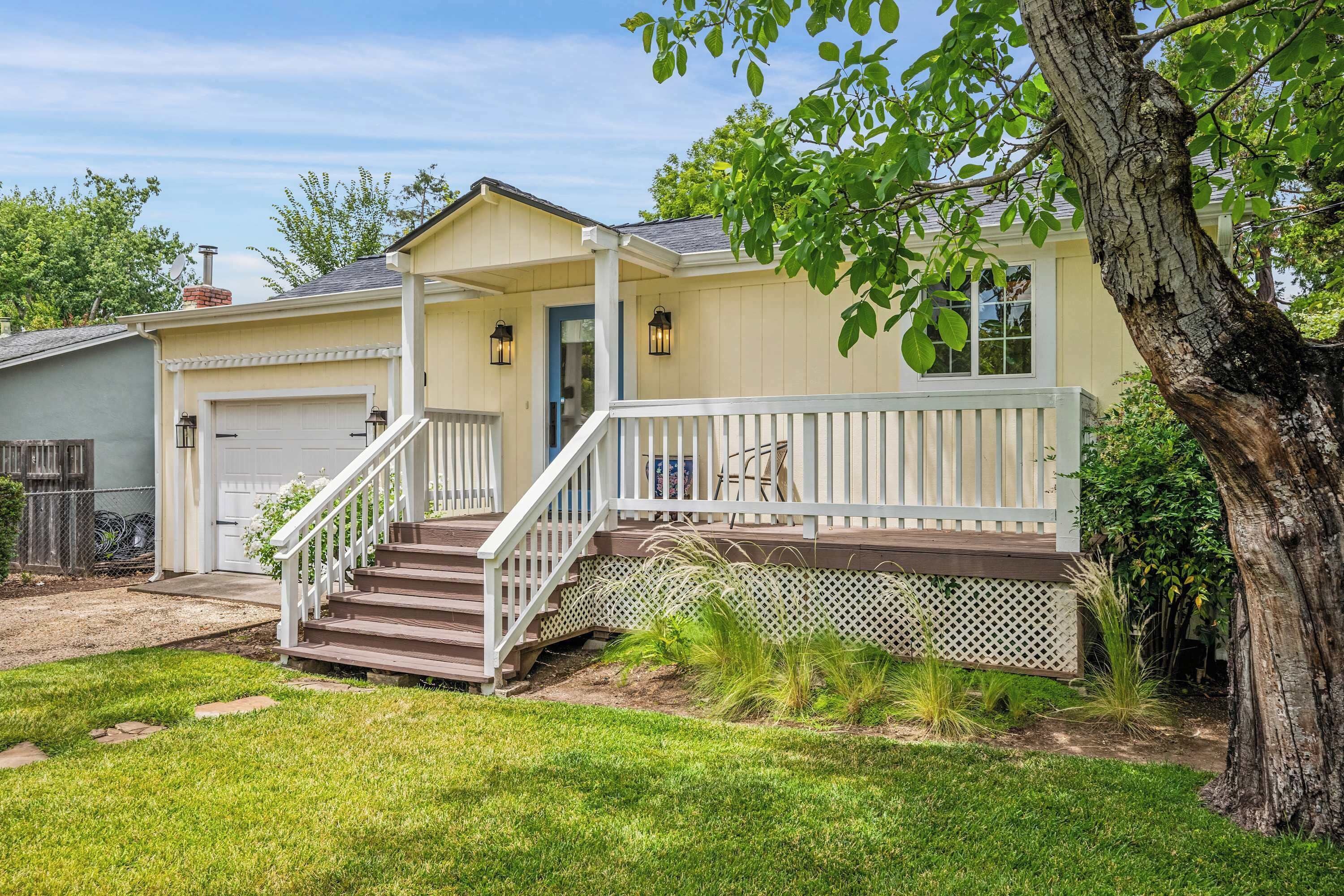 A two-story house with a front porch, a garage, and a tree in the yard.