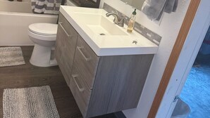 Une salle de bain avec un lavabo blanc, un miroir, un porte-serviettes, un rideau de douche et des toilettes.