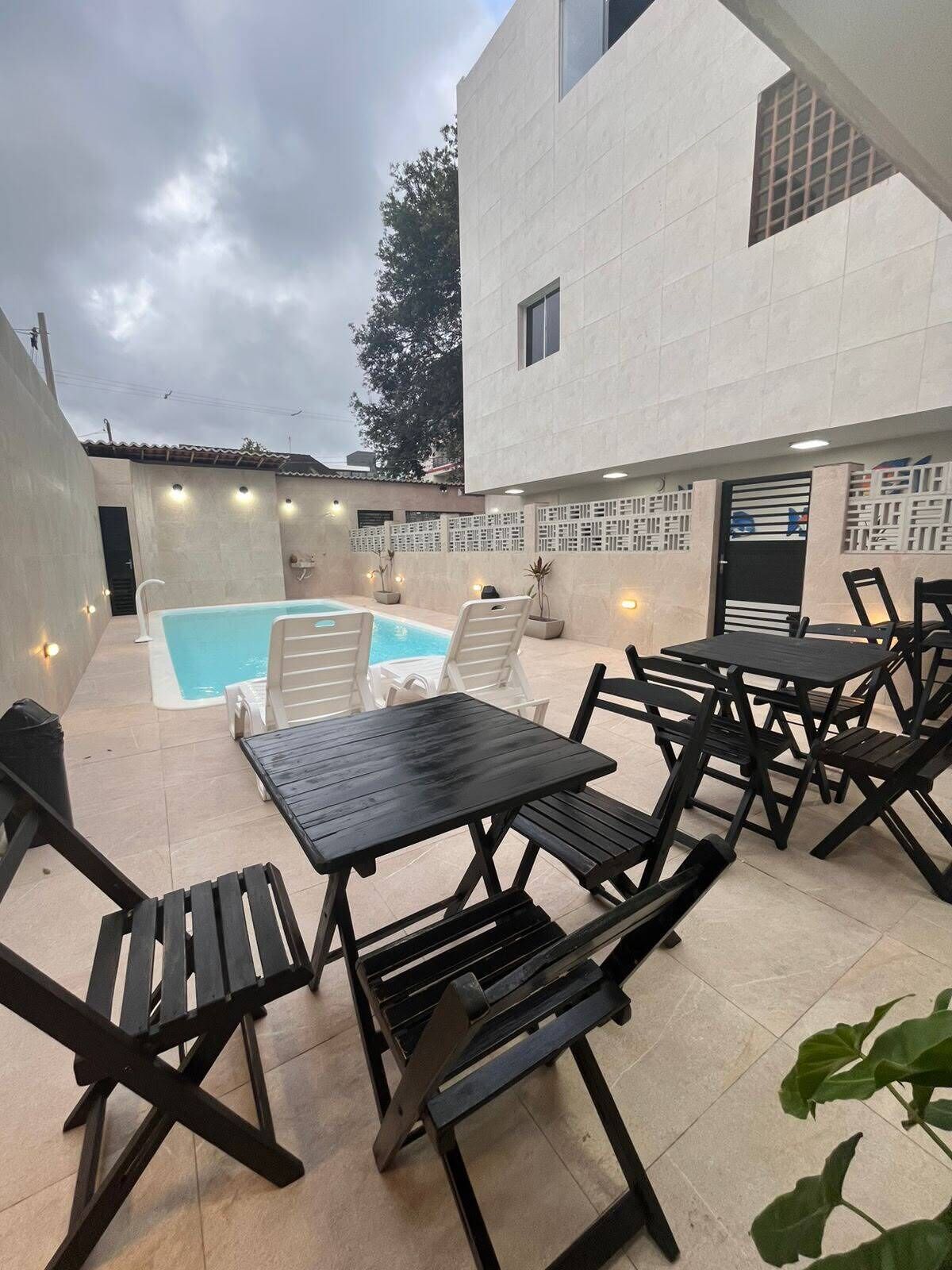 An outdoor patio with a pool, black metal furniture, and a white building with a door.