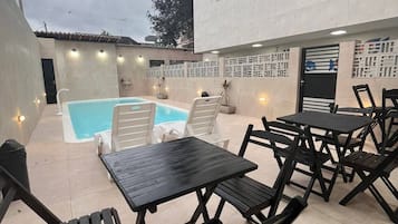 Um pátio externo com piscina, mobiliário de metal preto e um edifício branco com uma porta.