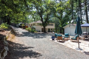 Ein Wohnhaus mit Schotterauffahrt, einer Sitzgelegenheit im Freien inklusive Stühle und Tisch sowie einer Garage mit Satellitenschüsseln.