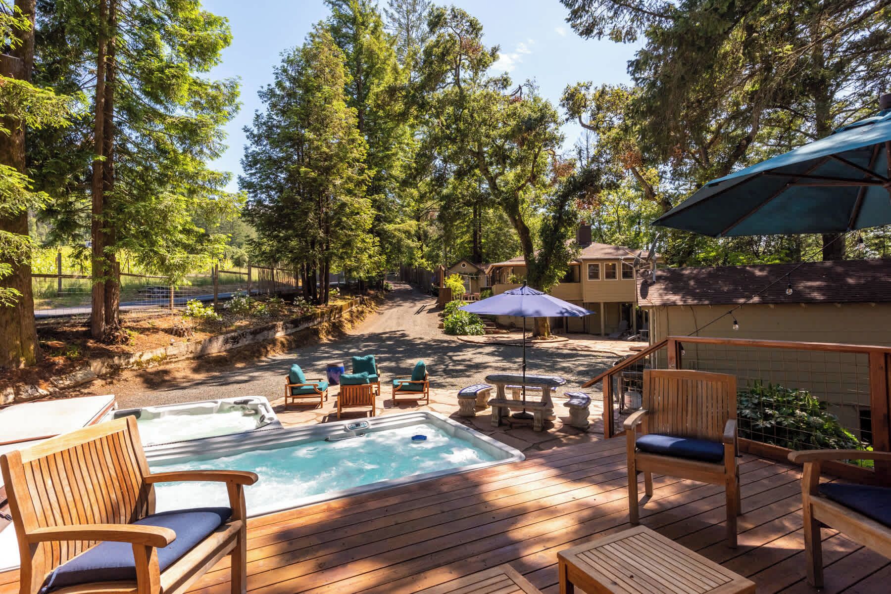 A wooden deck with a hot tub, outdoor furniture, and a view of a residential area with trees and houses.