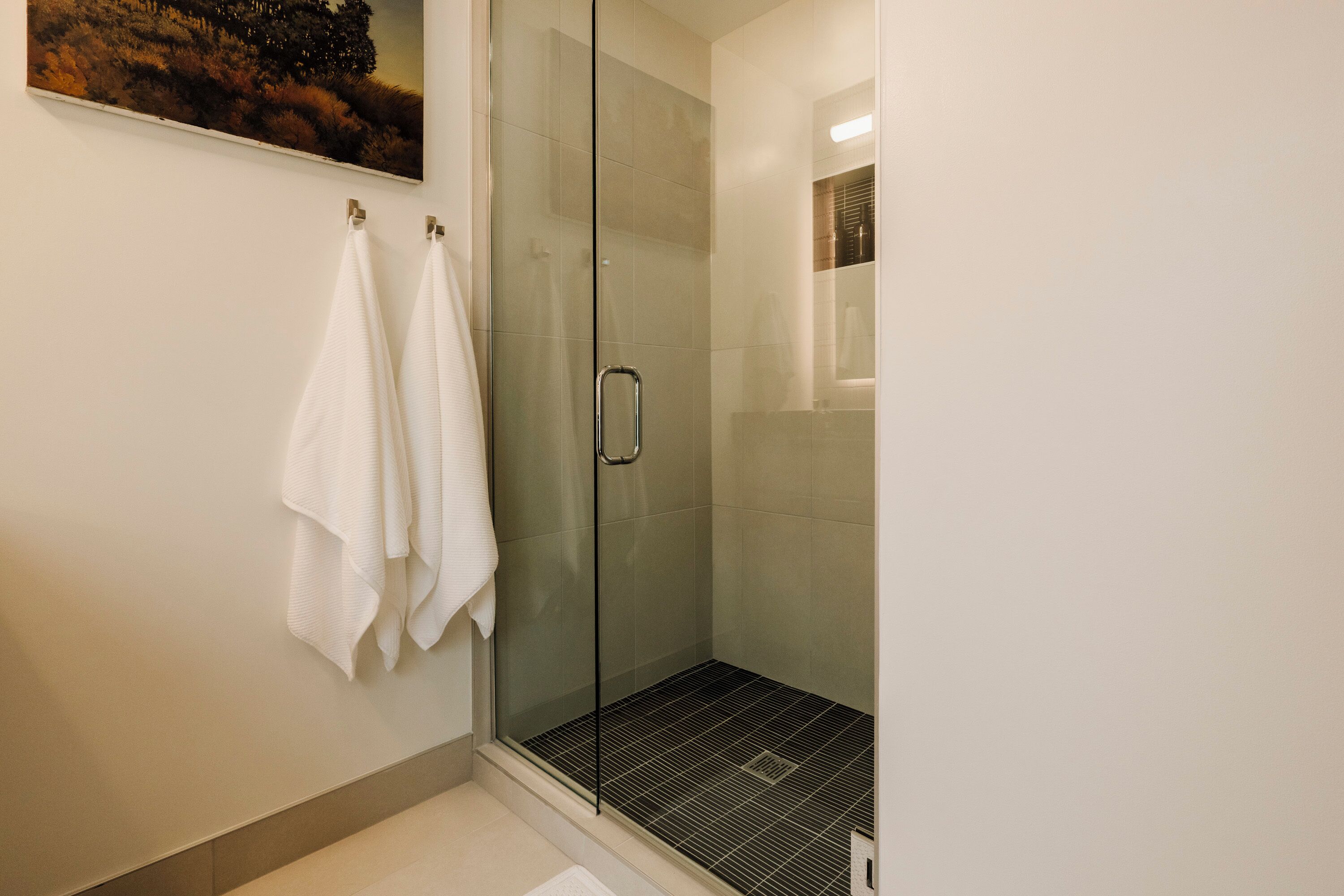 A modern bathroom with a glass shower enclosure, a white towel hanging on the wall, and a tiled floor.