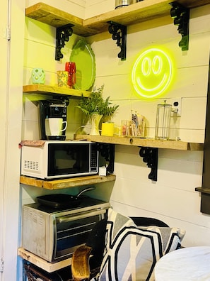 A kitchen with a neon smiley face, a coffee maker, a microwave, a toaster, and various kitchen utensils.