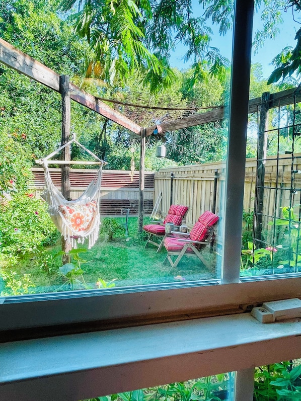 A glass-enclosed patio with a hammock, two red-striped chairs, and a wooden deck.