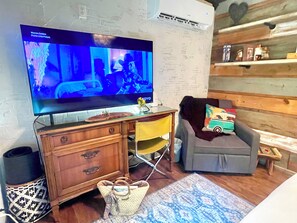 A living room with a flat-screen TV, wooden furniture, a patterned rug, and a small table with decorative items.