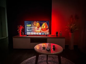 A modern living room with a flat-screen TV on a white entertainment unit, a glass coffee table, and decorative items. - Hodo Apartments | Modern Cozy Apartment in Tirana 15 mins away from city Centre! (Tiranë)