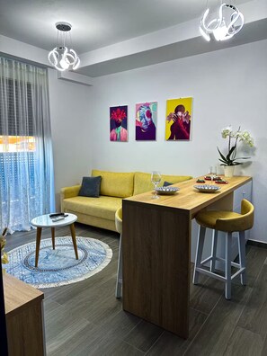 Een moderne woonkamer met een gele bank, een houten eettafel en drie abstracte schilderijen aan de muur.
