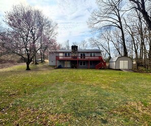 A two-story house with a red balcony, a stone chimney, and a garage. - Stunning view of the North Golf Course from the back deck. (Cherokee Village)