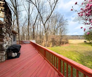 A wooden deck with a stone wall, a covered grill, and a view of a grassy field with trees. - Stunning view of the North Golf Course from the back deck. (Cherokee Village)