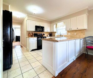 A kitchen with white cabinetry, a black refrigerator, and a tiled floor. - Stunning view of the North Golf Course from the back deck. (Cherokee Village)