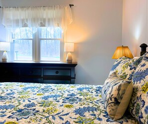 A bedroom with a bed, two bedside lamps, a window with sheer curtains, and a view of trees outside. - Stunning view of the North Golf Course from the back deck. (Cherokee Village)