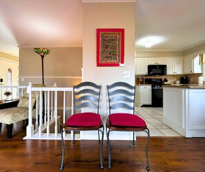 A dining area with two chairs, a staircase, a kitchen with white cabinets, and a decorative wall piece. - Stunning view of the North Golf Course from the back deck. (Cherokee Village)