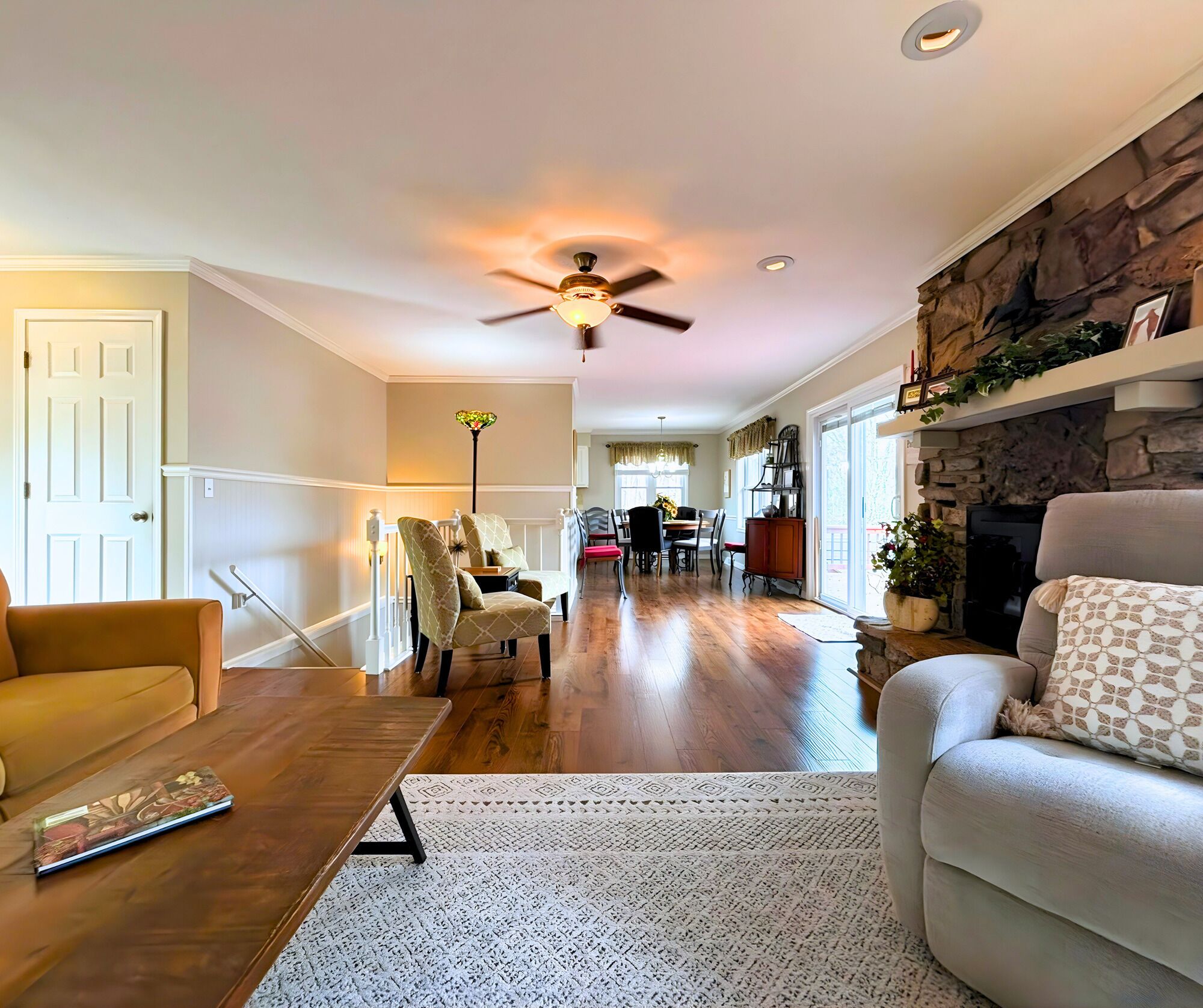 A spacious living room with hardwood flooring, a ceiling fan, and a fireplace.