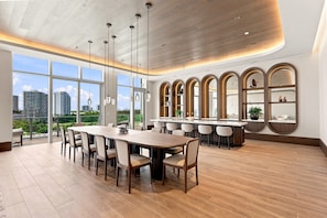 Uma área de refeições moderna com uma grande mesa de madeira e cadeiras, uma cozinha com bancada e grandes janelas com vista para a cidade.