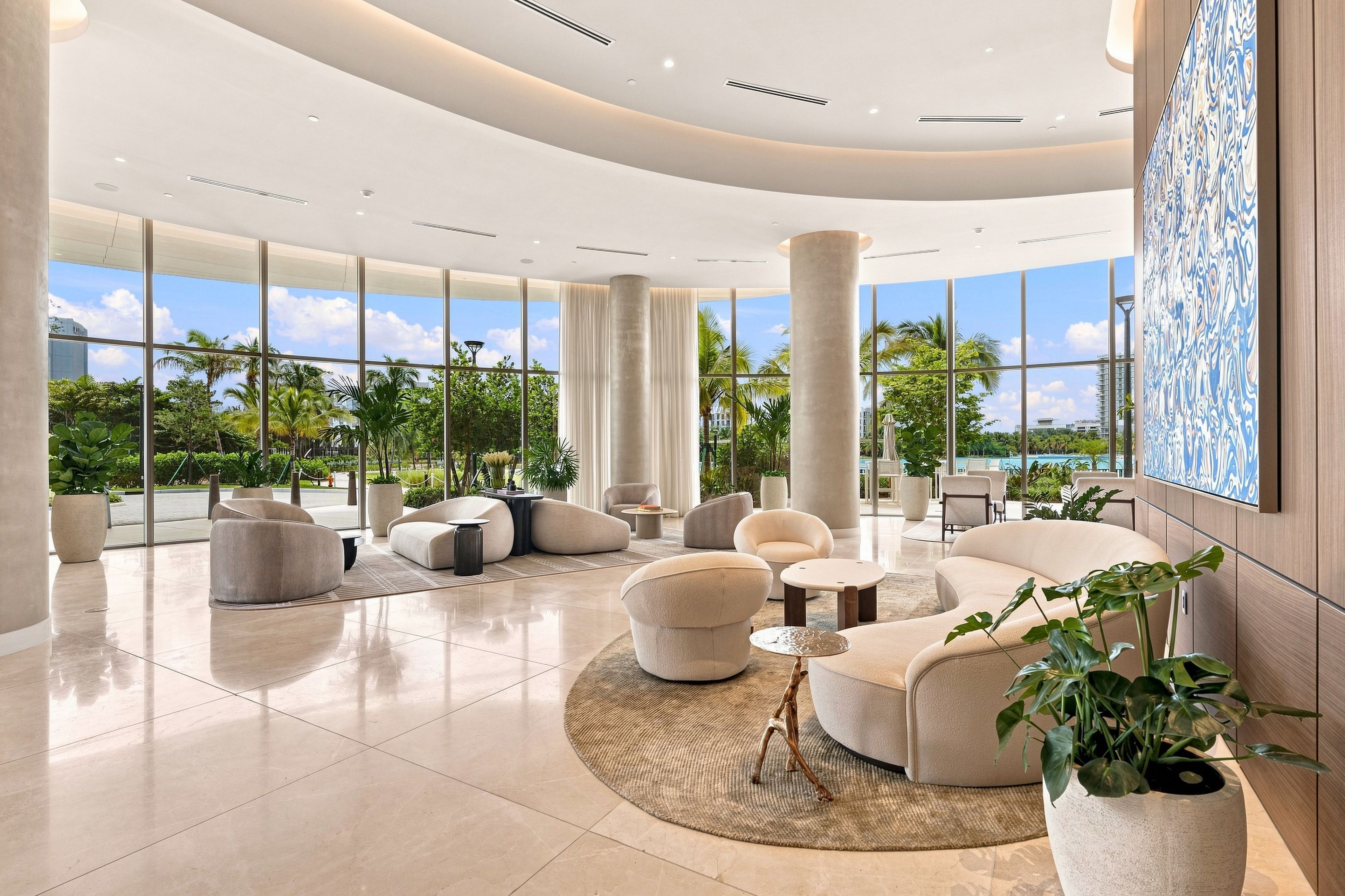 A spacious lobby with a curved ceiling, large windows offering a view of palm trees and a pool, and modern seating arrangements.