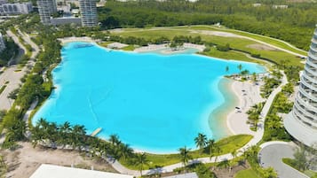 Uma piscina grande e límpida, azul, rodeada por palmeiras e com um horizonte urbano ao fundo.