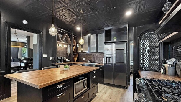 Een moderne keuken met donkere kastjes, een houten eiland, roestvrijstalen apparatuur en een decoratief plafond.