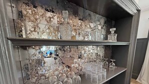 Een bar met een marmeren achterwand en planken vol glazen en flessen.