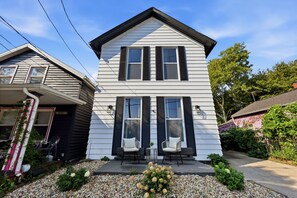 A two-story house with a front porch, a small garden, and a neighboring house. - Heart of Ohio City, Sleeps 8 & Fenced Yard (Cleveland)
