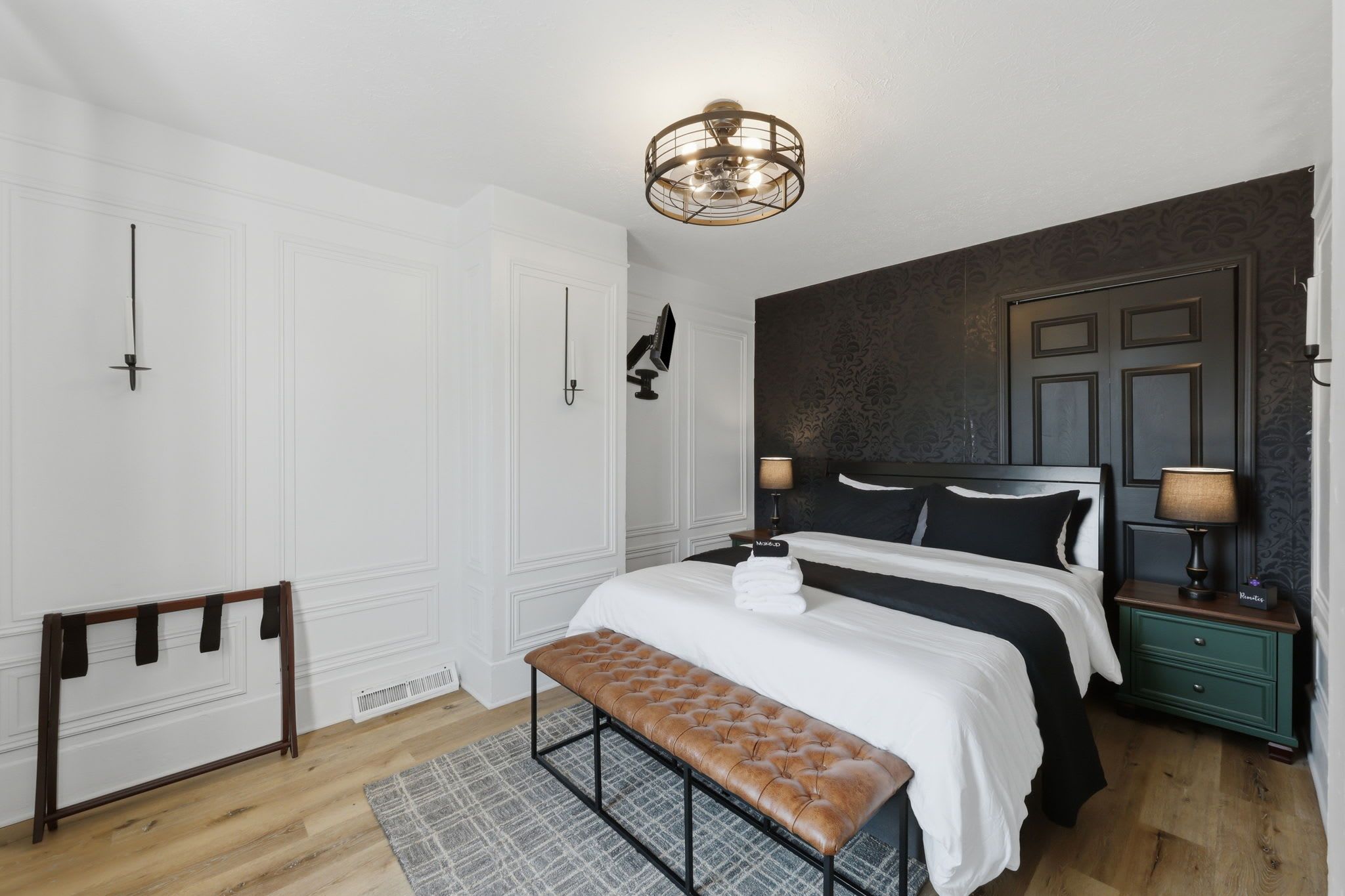 A bedroom with a bed, bench, bedside tables, and a ceiling light fixture.