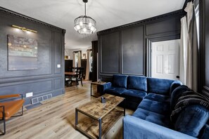Ein modernes Wohnzimmer mit einem dunkelblauen Ecksofa, einem Holztisch und einem Essbereich im Hintergrund.