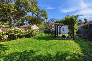 Un jardin avec une pergola en bois, un foyer extérieur et une pelouse verdoyante.