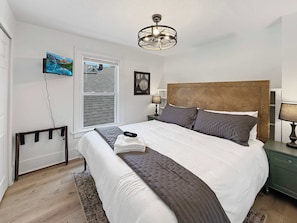 Ein Schlafzimmer mit einem Bett, einem Nachttisch, einer Lampe, einem Deckenventilator, einem Fenster und einem an der Wand montierten Fernseher.