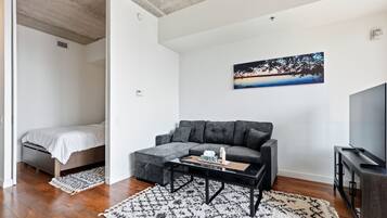 A modern living room with a grey sofa, a coffee table, a TV, and a painting on the wall.