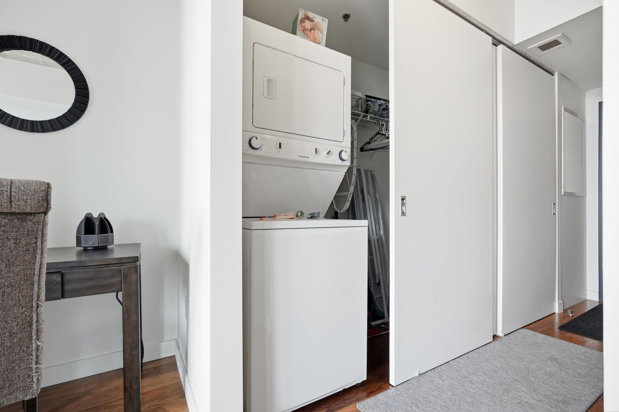 A laundry area with a washing machine and dryer, a small table with a towel, and a mirror on the wall.