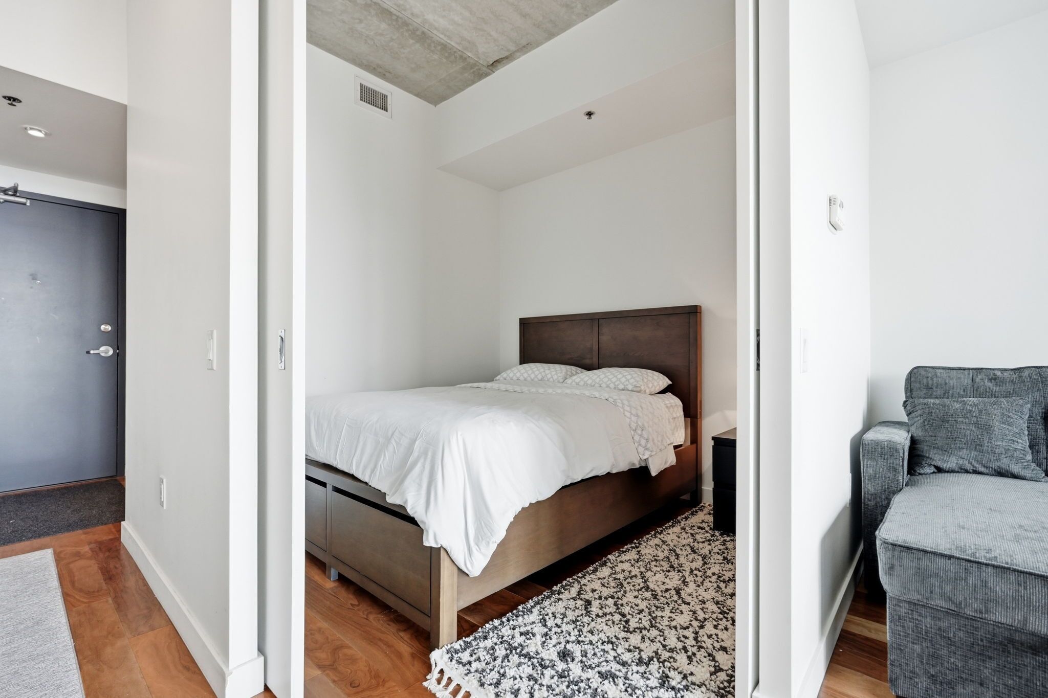 A bedroom with a bed, a grey armchair, and a patterned rug.