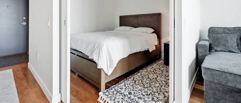 A bedroom with a bed, a grey armchair, and a patterned rug.
