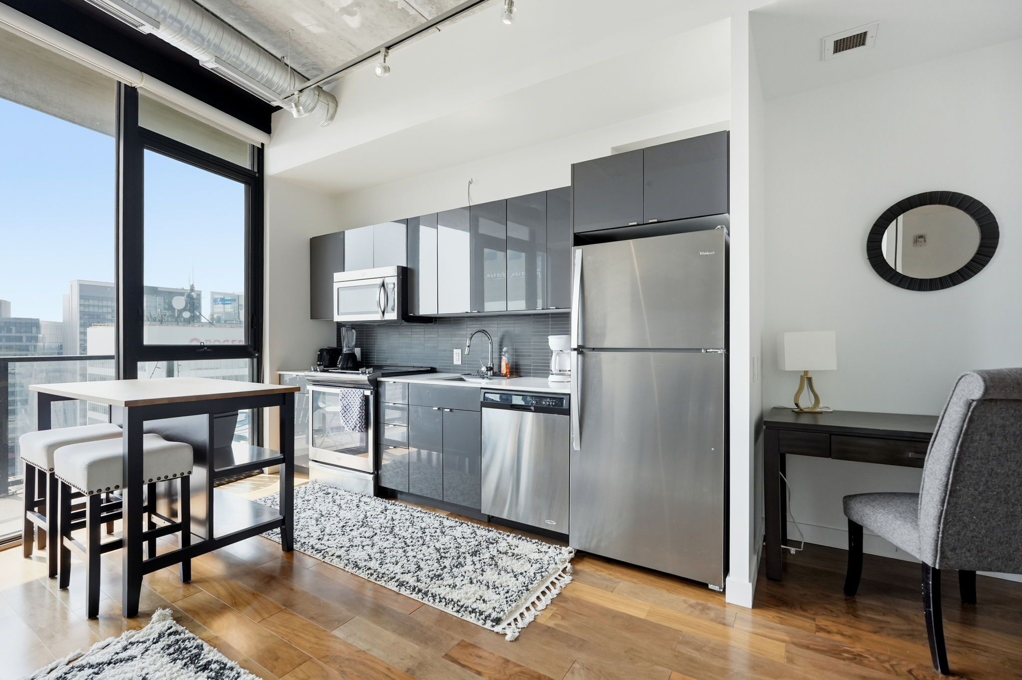 A modern kitchen with stainless steel appliances, a dining area with a table and chairs, and a view of the city through large windows.