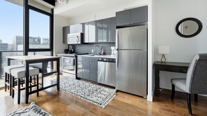 Une cuisine moderne équipée d’appareils électroménagers en acier inoxydable, un coin repas avec une table et des chaises, et une vue sur la ville grâce à de grandes fenêtres.