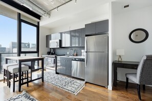 Eine moderne Küche mit Edelstahlgeräten, ein Essbereich mit Tisch und Stühlen sowie ein Blick auf die Stadt durch große Fenster.