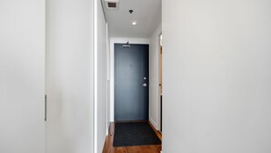 Un couloir étroit, avec une porte bleu foncé au fond, des murs blancs et un paillasson noir à l’entrée.
