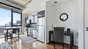 A modern kitchen with stainless steel appliances, a dining area with a table and chairs, and a large window offering a city view.