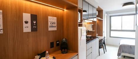 Una cocina moderna con muebles de madera, un espacio para café y una cama en la habitación contigua.