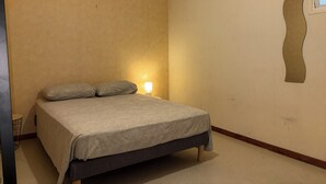 A bedroom with a bed, a nightstand, a lamp, and a window. - Apartment in Downtown Montluel (Montluel)