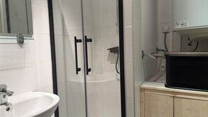 A bathroom with a glass-enclosed shower, a white sink, and a wooden cabinet. - Apartment in Downtown Montluel (Montluel)