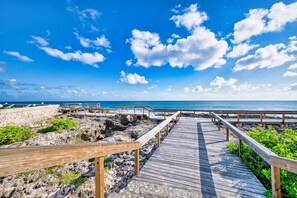 A wooden boardwalk leading to a beach with a clear blue sky and scattered clouds. - Oceanfront Peace 2BR with Wave Views (Patricks Island)