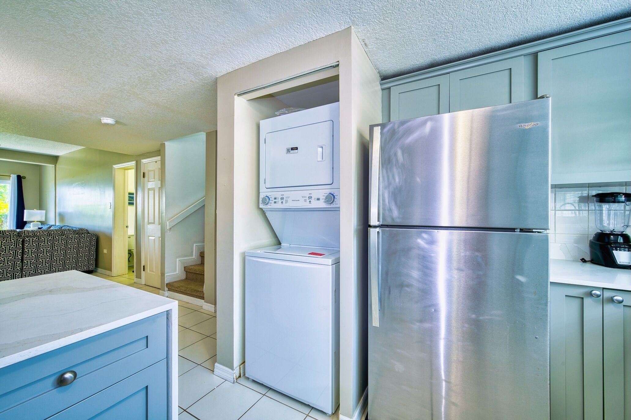Una cocina compacta con refrigerador de acero inoxidable, lavadora-secadora integrada y una licuadora sobre la encimera.